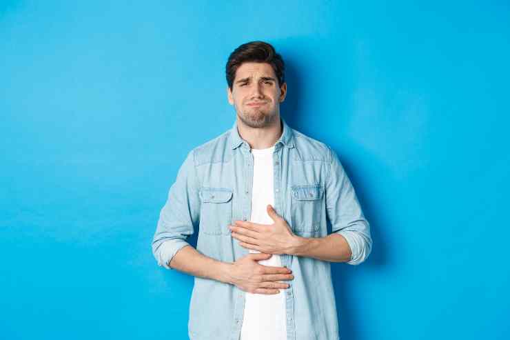 Man Holding Hands Belly Grimacing From Pain Complaining Stomach Ache Standing Against Blue Background 1